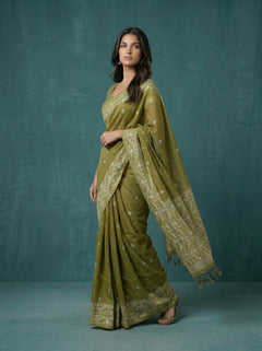 Woman wearing a green saree with a matching blouse against a teal background