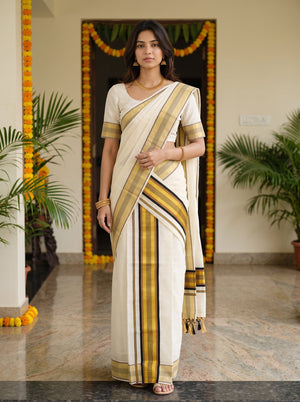 A woman modeling a traditional Indian saree in an indoor setting with marble flooring and potted plants. The saree is off-white/cream with prominent vertical stripes in black, mustard yellow, and brown, paired with a matching cream blouse.