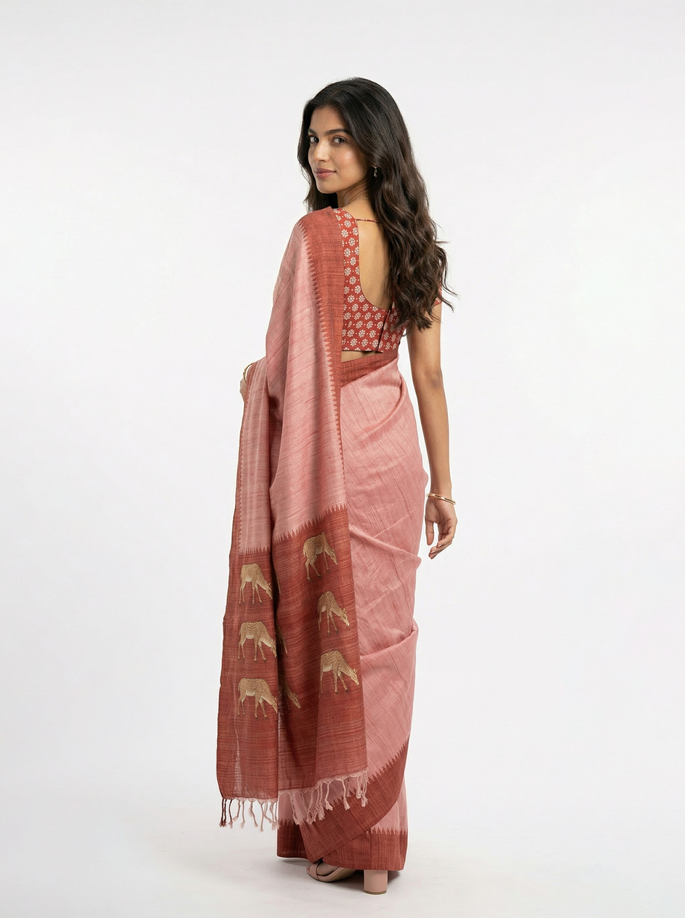 Woman in a pink saree standing in a room with decorative elements.