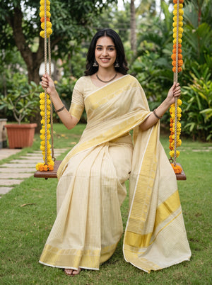 A woman wearing a cream and yellow striped cotton saree sits on a swing in a lush green garden. She is holding yellow marigold garlands, and the background features a well-maintained lawn and tropical foliage.