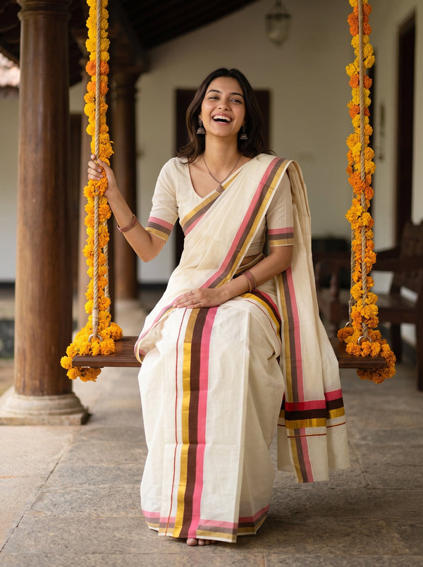 A woman wearing a cream-colored cotton saree with pink, yellow, and green stripes sits on a wooden swing decorated with marigold garlands in a traditional courtyard.