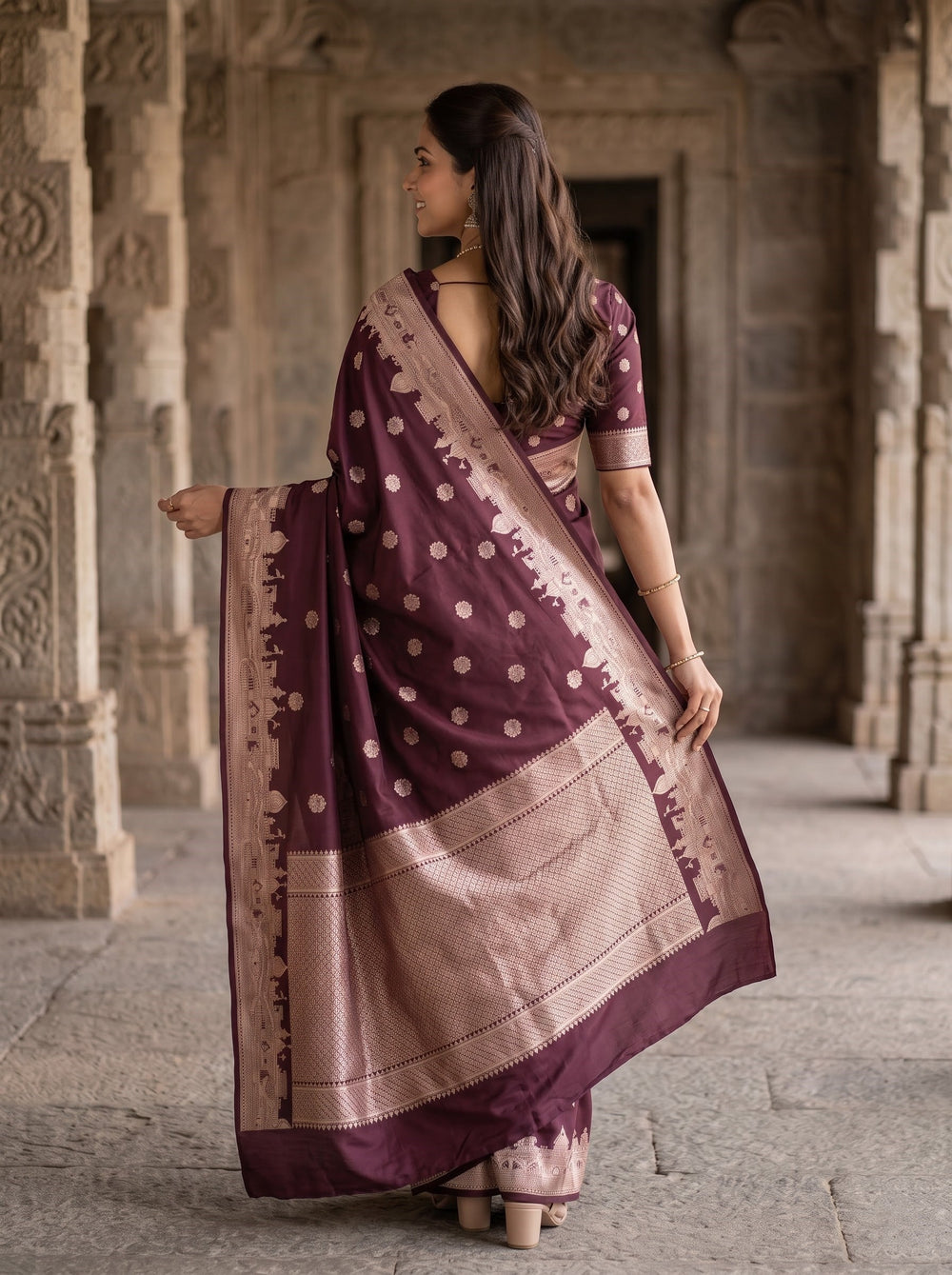 A woman wearing a deep purple and beige Banarasi silk saree with gold polka dots and a detailed beige border, standing in a stone corridor.