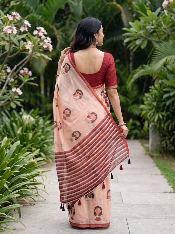 A woman viewed from behind wearing a peach and rust-colored printed saree with a red blouse, standing on a stone path surrounded by lush green garden foliage.
