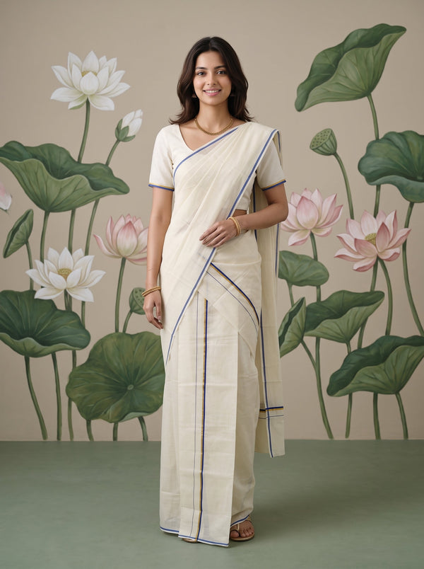 A woman modeling a cream-colored cotton saree with thin blue and green border stripes, paired with a matching cream blouse, standing in front of a painted lotus wall mural.