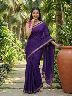 Woman in a purple saree standing outdoors with greenery in the background