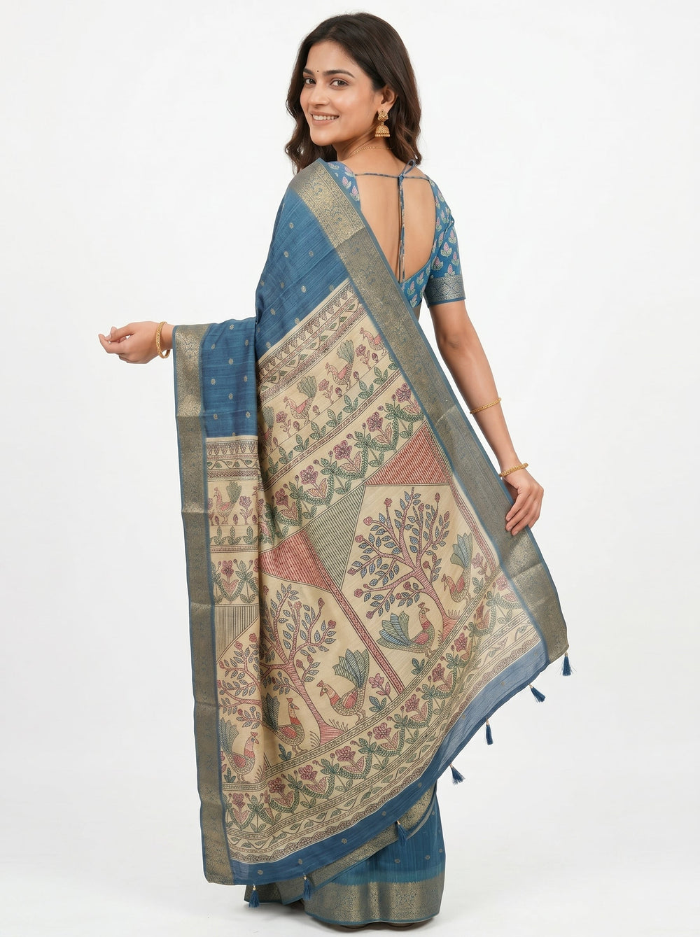 Woman in a blue saree with intricate patterns standing against a textured wall.