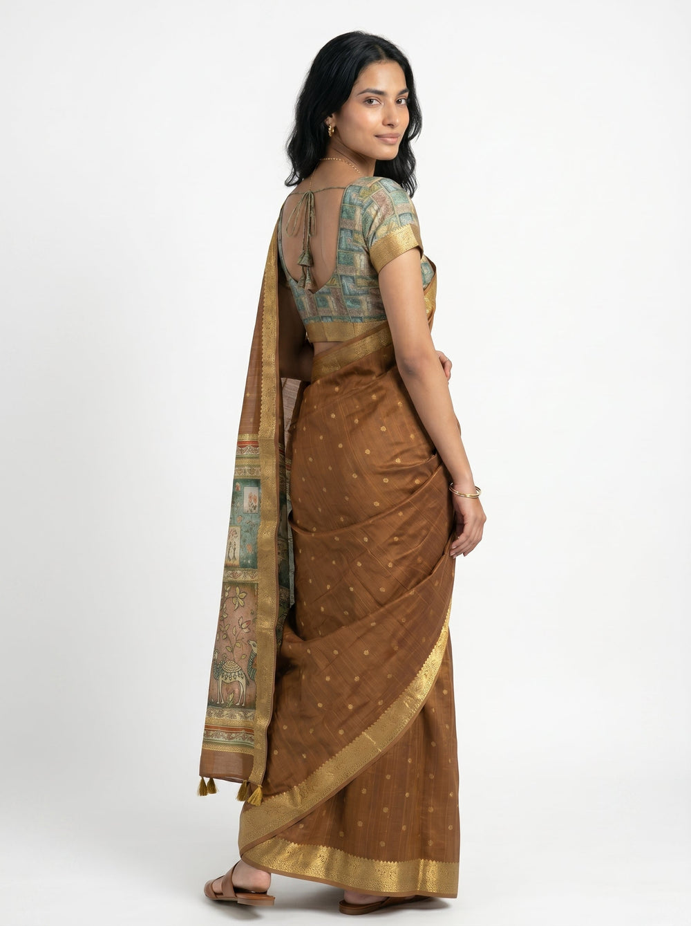 Woman in a traditional saree holding flowers, standing in a doorway with greenery outside.
