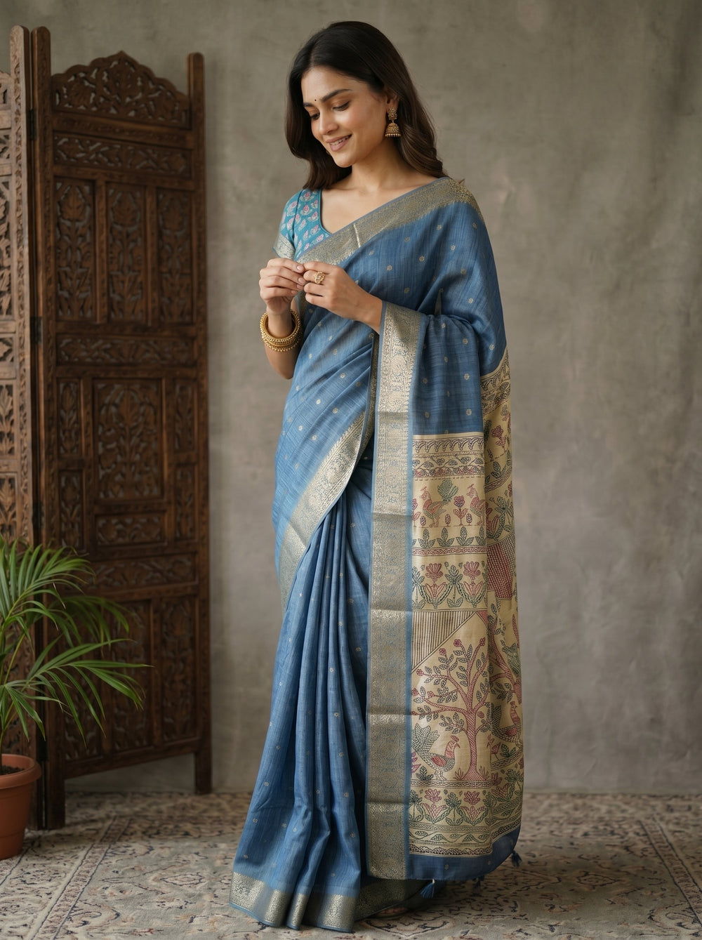 Woman in a blue saree with intricate patterns standing against a textured wall.