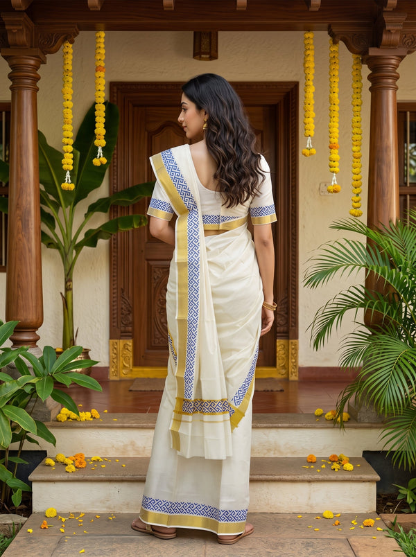 A woman wearing a traditional Indian saree stands on the steps of a porch, viewed from behind. The saree is off-white/cream with blue and yellow patterned borders.