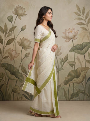 A woman modeling a white saree with olive green borders and a matching green-trimmed blouse, standing in front of a beige floral wall mural.