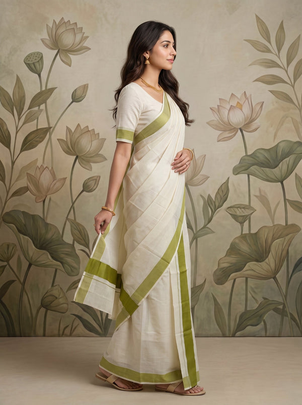 A woman modeling a white saree with olive green borders and a matching green-trimmed blouse, standing in front of a beige floral wall mural.