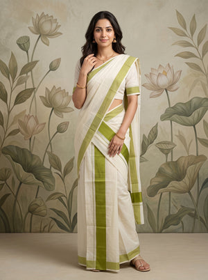 A woman modeling a white and olive green saree with a matching short-sleeve blouse, standing against a beige wall with a floral lotus pattern.
