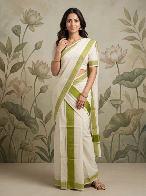 A woman modeling a white and olive green saree with a matching short-sleeve blouse, standing against a beige wall with a floral lotus pattern.