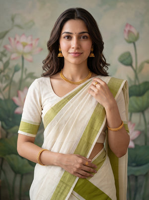 A woman wearing a white and olive green saree with gold jewelry, standing in front of a painted lotus pond backdrop.