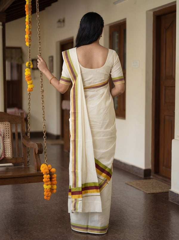 A woman viewed from behind wearing a cream-colored cotton saree with a matching short-sleeve blouse. The saree features thin stripes of green, yellow, and red along the border and pallu.