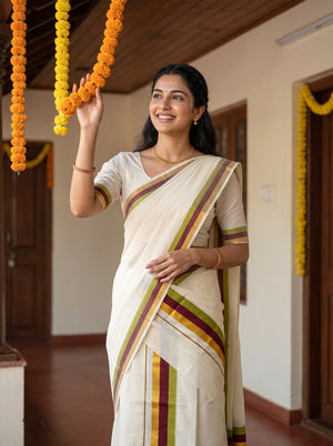 A woman wearing a cream-colored traditional Indian saree with green, yellow, and maroon stripes, standing in a decorated indoor hallway and holding a yellow marigold garland.