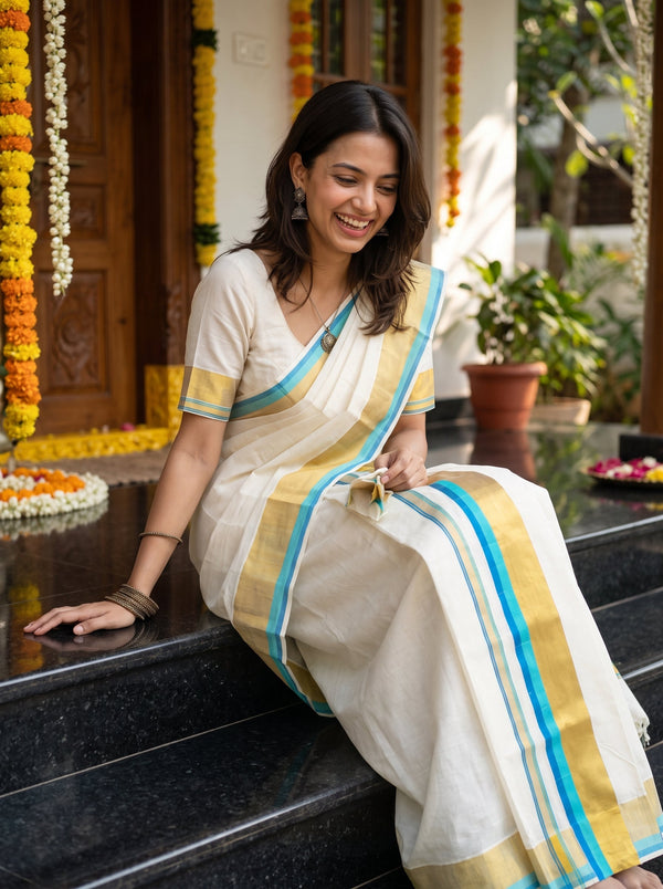 A woman wearing a cream-colored cotton saree with blue and mustard yellow stripes sits on black marble steps in front of a decorated doorway.