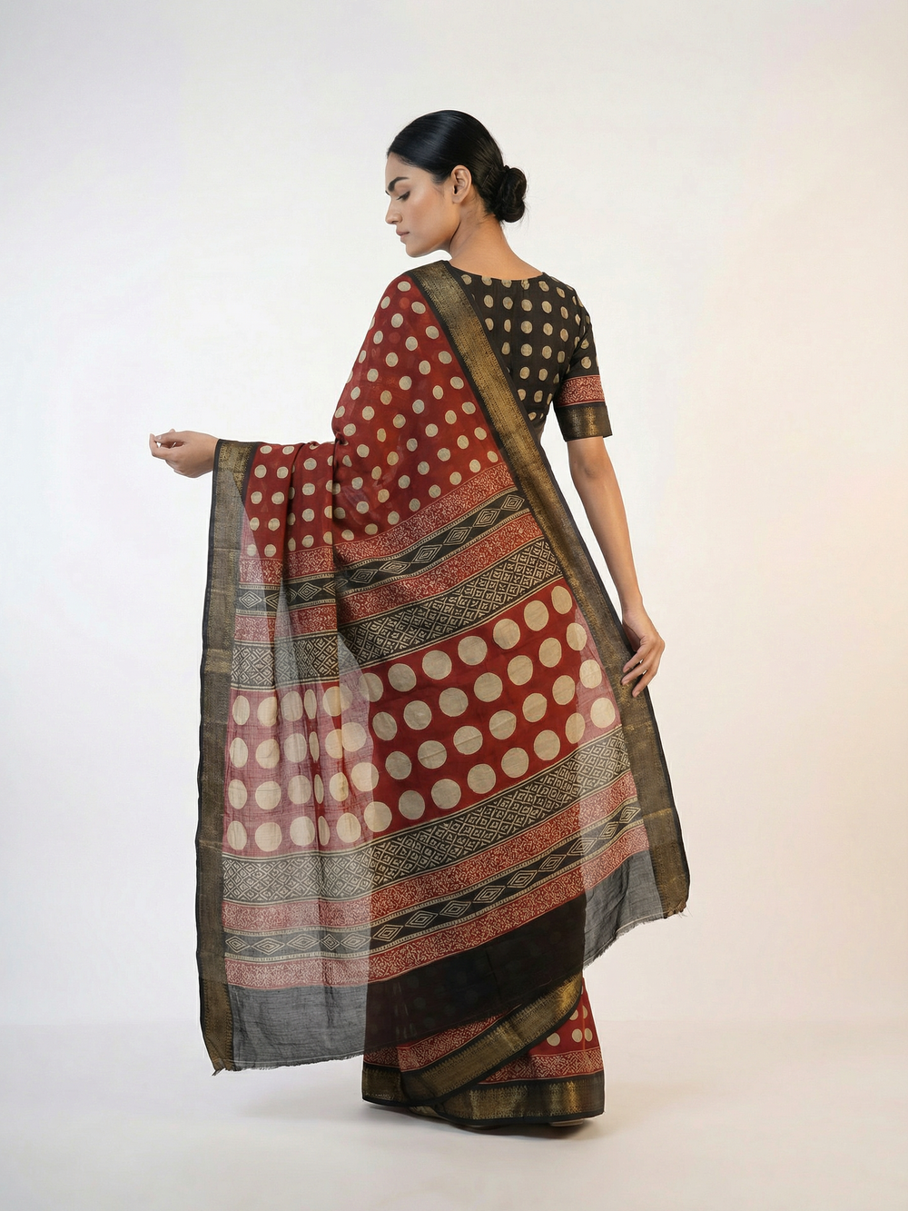Woman wearing a traditional saree with a patterned design against an old stone wall.