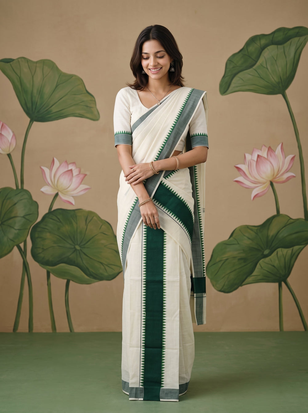 A woman modeling a traditional Indian saree with a white body, dark green border stripes, and a matching white blouse with green trim, posed against a beige backdrop with painted lotus leaves and flowers.