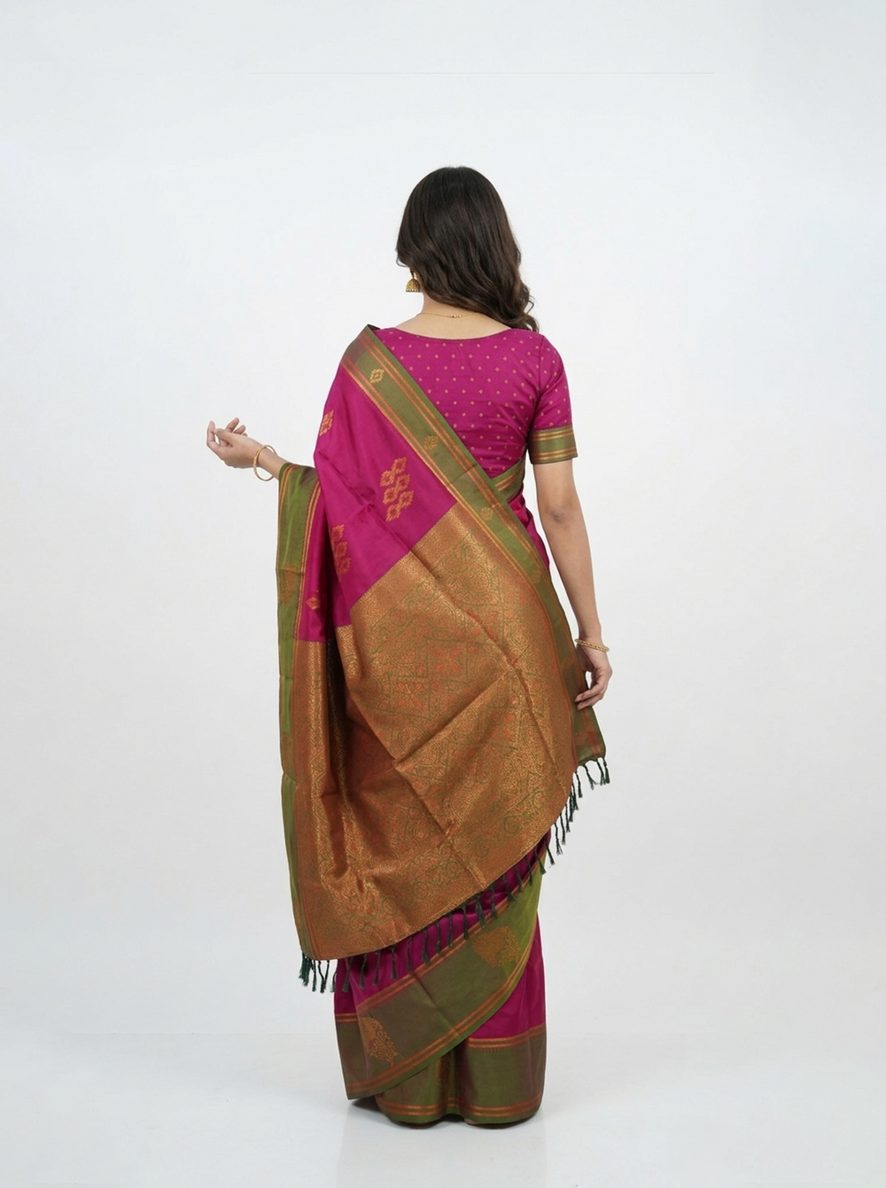Woman in a traditional saree standing in a room with wooden furniture and a mirror.