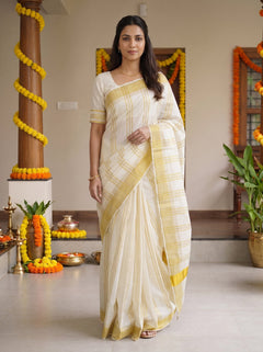 A woman modeling a cream and yellow checkered cotton saree in a decorated indoor setting with marigold garlands.