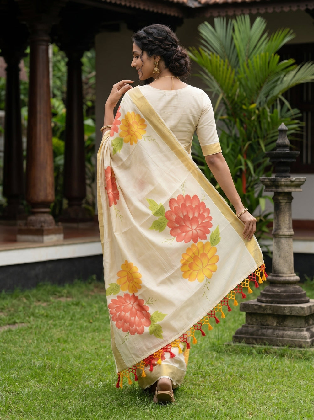 Woman in a floral saree standing outdoors with greenery and a traditional structure in the background