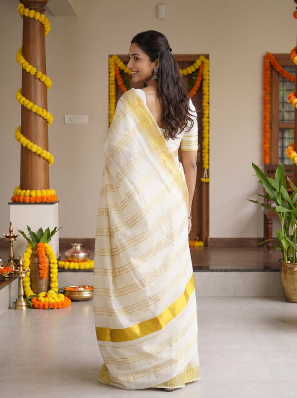 A woman wearing a white and yellow striped saree with a yellow border, standing in a decorated indoor space with marigold garlands.