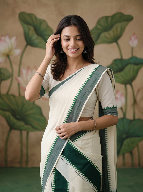 A woman wearing a cream and dark green saree with a matching short-sleeve blouse, standing in front of a decorative lotus leaf backdrop.