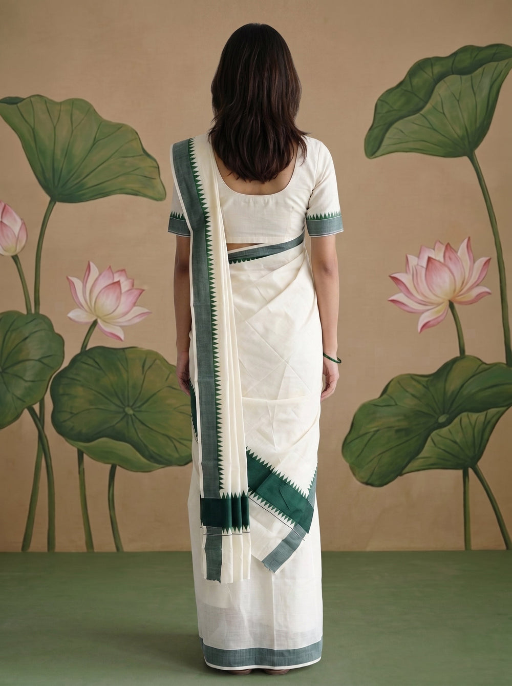 A woman modeling a traditional Indian saree with a white body, dark green border stripes, and a matching white blouse with green trim, posed against a beige backdrop with painted lotus leaves and flowers.