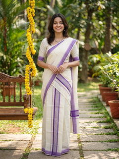 A woman wearing a white and purple saree stands on a stone path in a garden, with a wooden swing and yellow flower garlands visible on the left.