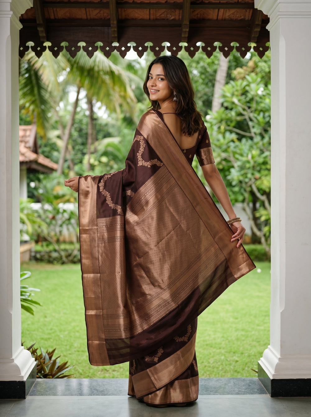 Woman in a brown saree standing outdoors with greenery in the background