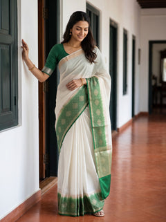 A woman wearing a white and green saree stands in a hallway with white walls and dark door frames, holding onto a wall for support.