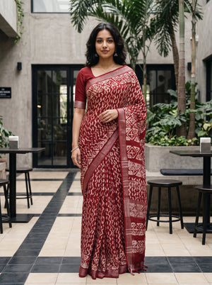 A woman modeling a red and white patterned saree in an outdoor patio setting with plants and tables.