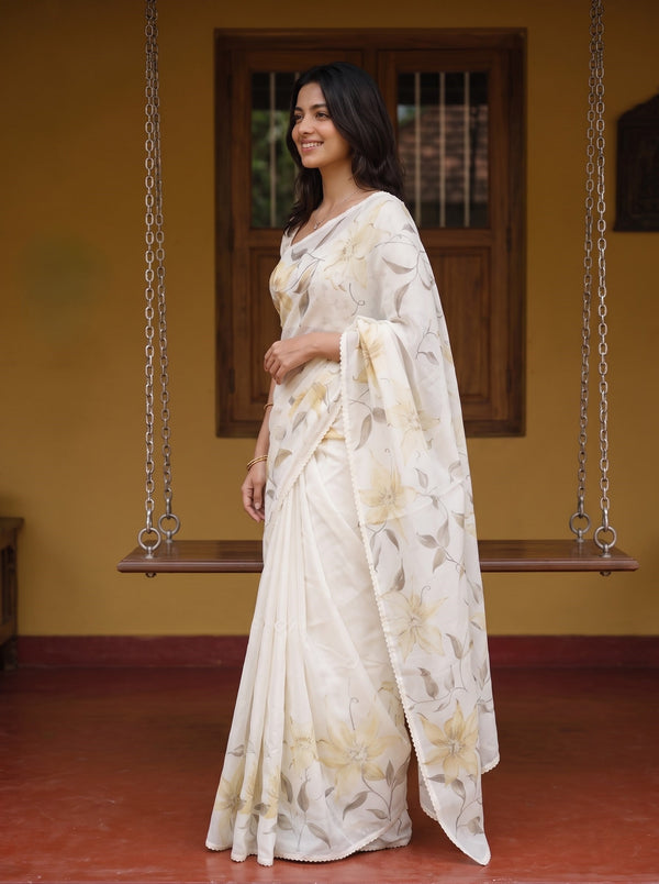 A woman wearing a cream-colored floral saree stands in profile in front of a rustic wooden swing and yellow wall.