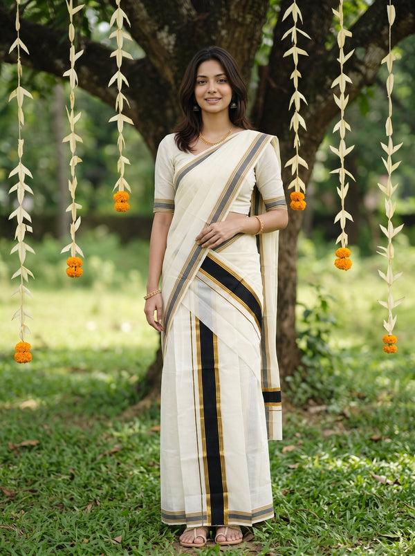 A woman wearing a cream-colored cotton saree with black and gold stripes, standing outdoors in front of a tree with hanging marigold garlands.